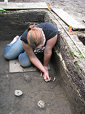 A field school student carefully excavates a white clay pipe.